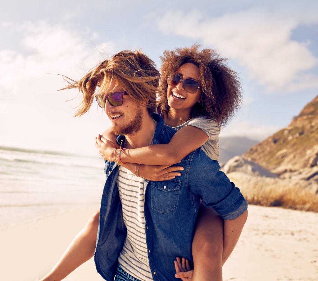 Young Couple Playing Piggyback On Beach